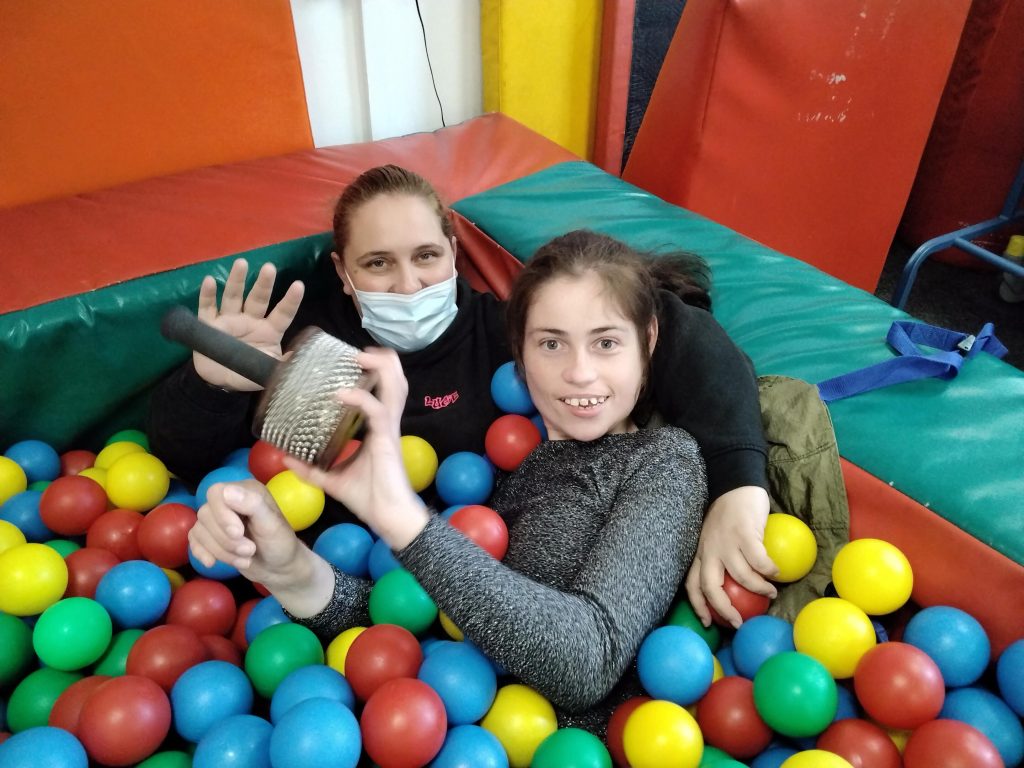 Young female individual laying in a ball pit with support worker