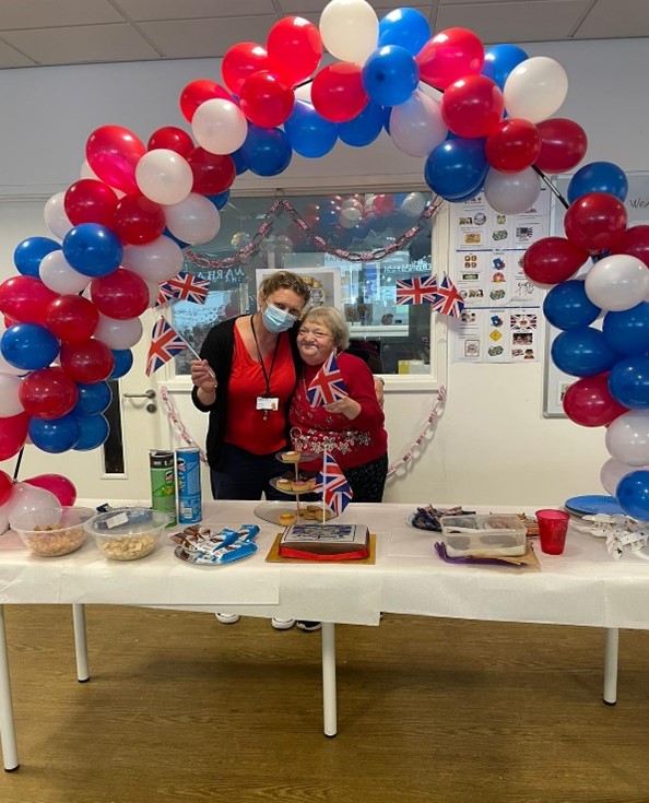 Staff and individuals we support celebrating under a red, blue and white balloon arch