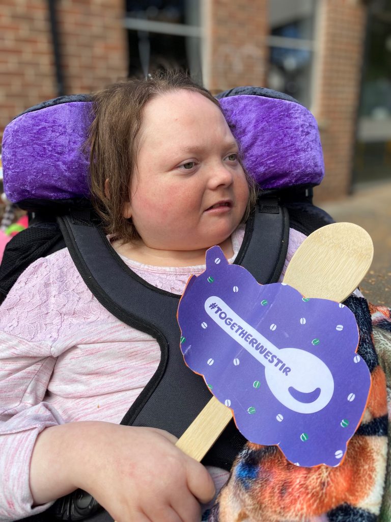 Female wheelchair user holding a togetherwestir wooden spoon