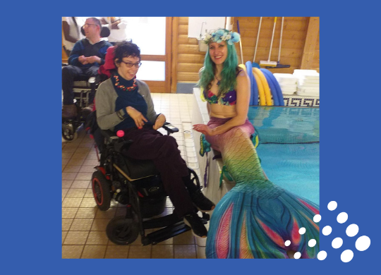 Mermaid sitting poolside with an individual wheelchair user beside her
