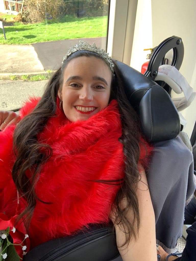 Princess Paige who is a wheelchair user wearing a red dress, red stole and tiara at her mum's wedding_Lewis Martin Court