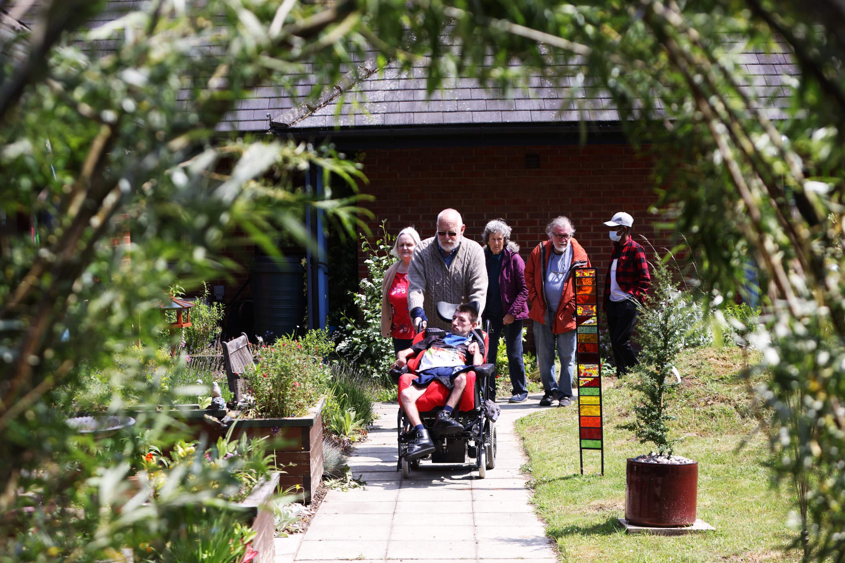 Group picture of individuals walking up the path of Birchwood Memorial Garden with one person pushing a wheelchair user