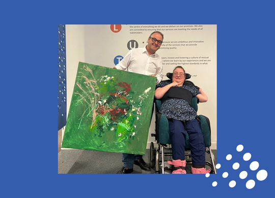 Elaine from Birchwood who is pictured sitting in her wheelchair with her painting being held by John Godden MBE who is standing along side her